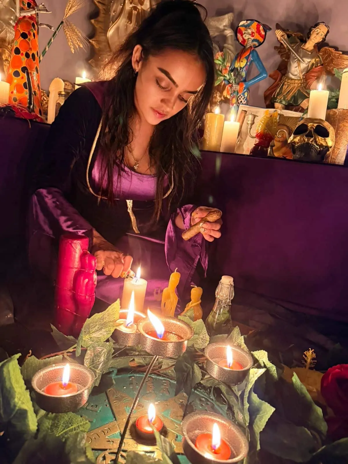 La Maestra Sara, con vestido morado, enciende una vela roja dentro de un círculo de velas frente al altar
