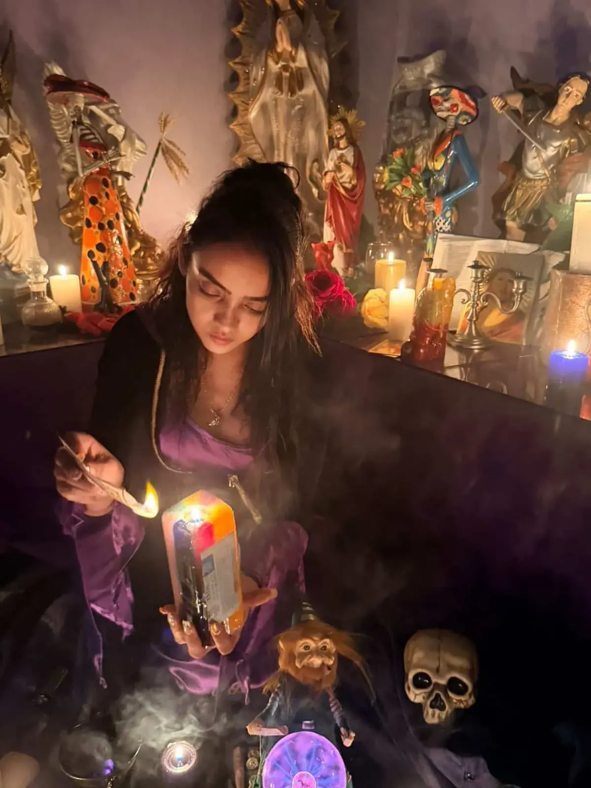 La Maestra Sara enciende con un cerillo una vela de colores frente a imágenes de santos